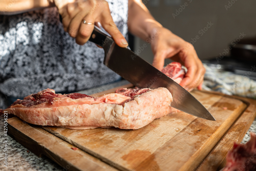 Woman in her kitchen cutting a piece of beef to prepare a meal.
