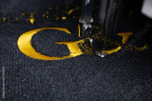 Machine embroidery on black velvet fabric with yellow thread. Embroidered initial G. Close up.