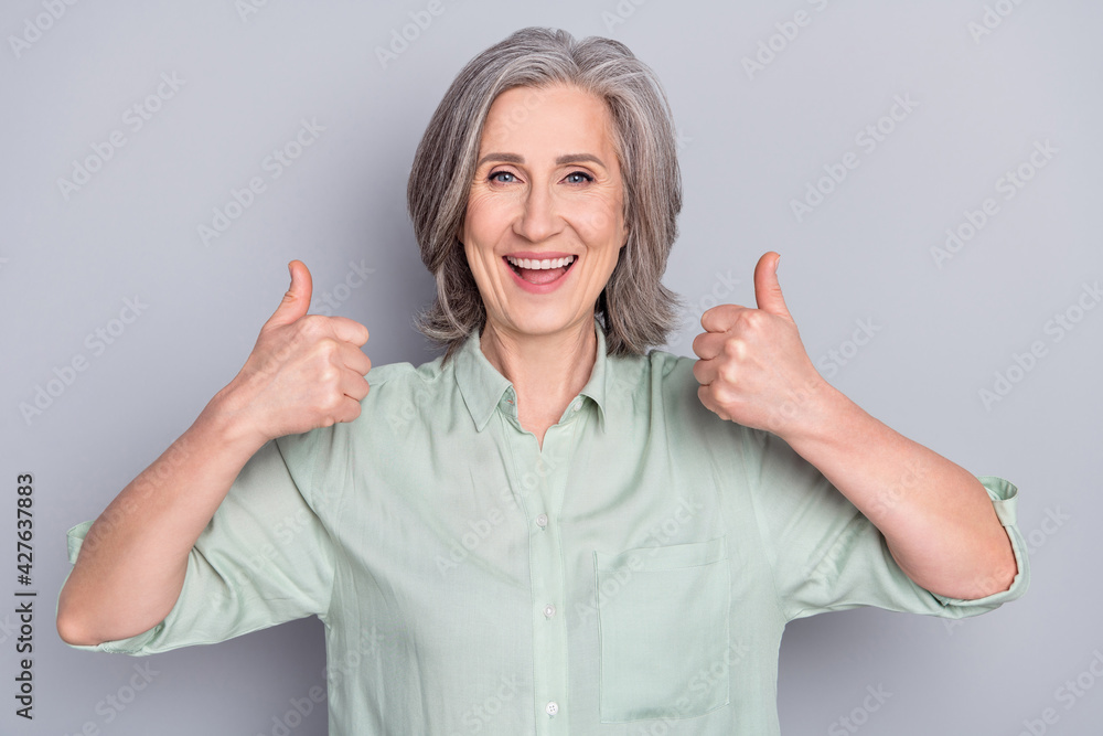 Photo of happy excited cheerful good mood mature woman showing thumb-up approval isolated on grey color background Photo of happy excited cheerful good mood mature woman showing thumb-up approval isolated on grey color background