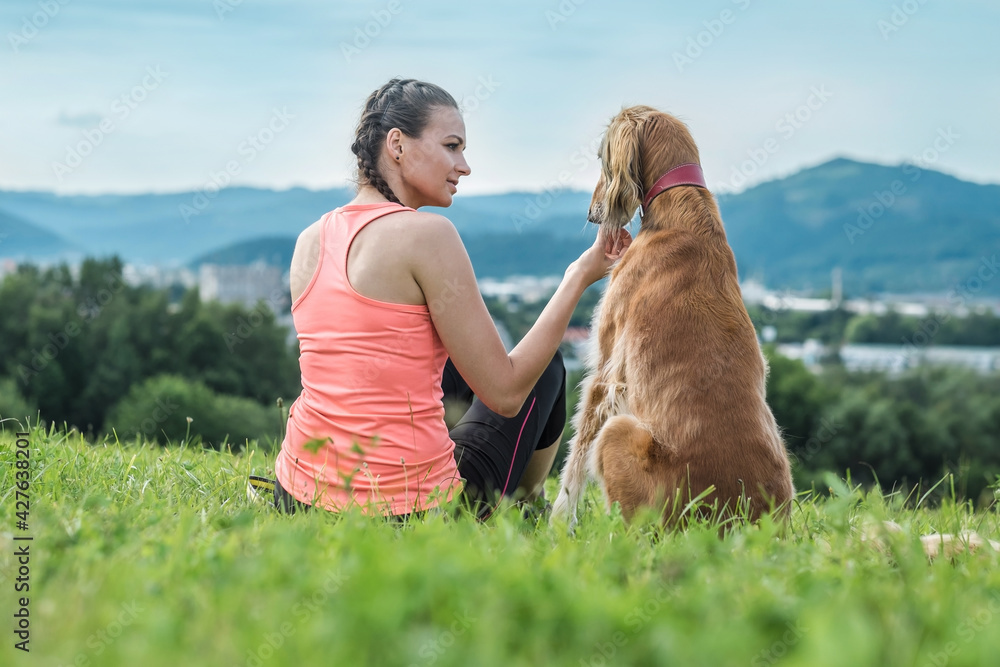 Woman runner and dog on field under golden sunset sky in evening time. Outdoor running. Athletic young man with his dog are running in nature.
