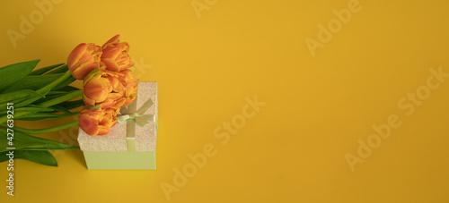 Orange-red fresh tulips in a bouquet and a gift box on a yellow background. Greetings  celebration  romance concept. Copy space. Bright colorful postcard for congratulations on all holidays and events