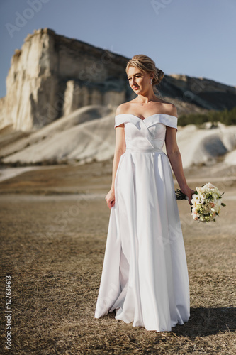 Beautiful bride in a wedding dress with a bouquet standing against white rock