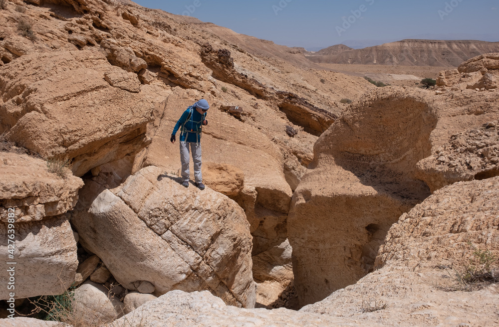 Hiking trail in dry wadi Tahmason, Judaean Desert, Southern Israel. Female hiker looking into a canyon above a narrow stone gate.