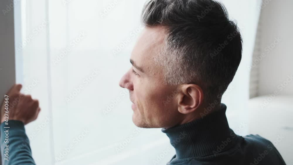 A side view of a mature man looking out the window in the kitchen A side view of a mature man looking out the window in the kitchen