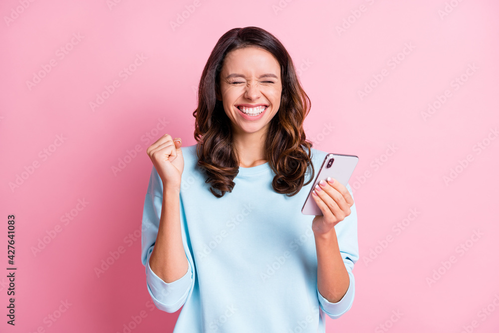 Photo of young excited crazy girl fists hand celebrate win victory success use cellphone isolated over pink color background Photo of young excited crazy girl fists hand celebrate win victory success use cellphone isolated over pink color background