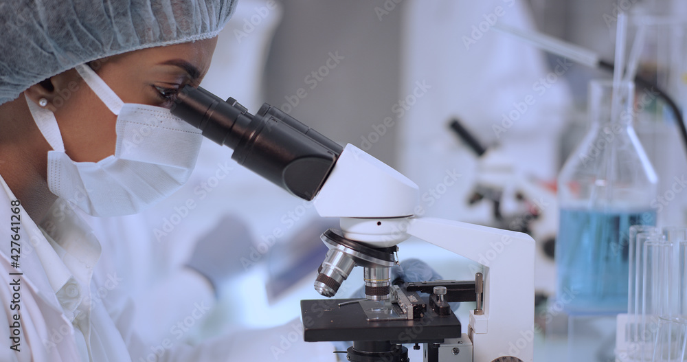 Worried female scientist studying medical samples. Team working in background Worried female scientist studying medical samples. Team working in background