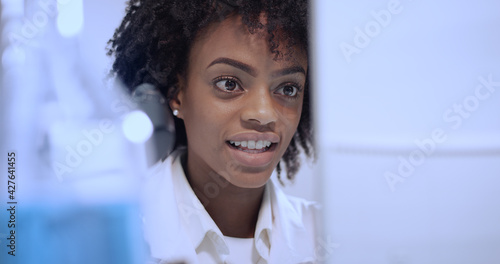 African ethnicity, female doctor using microscope in laboratory. Sitting in front of computer screen