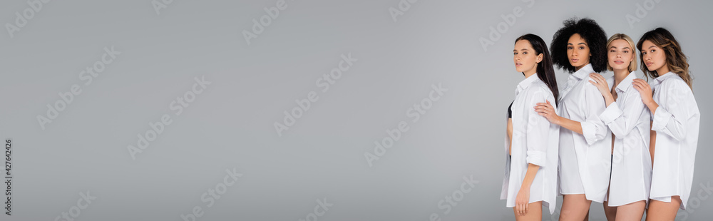 sexy interracial women in white shirts looking at camera isolated on grey, banner sexy interracial women in white shirts looking at camera isolated on grey, banner