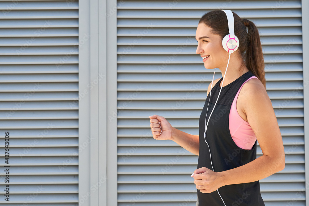 Beautiful sportive woman listens to music with headphones while jogging.