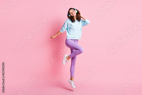 Full size photo of young beautiful girl happy smile crazy active listen music earphones jump isolated over pastel color background © deagreez