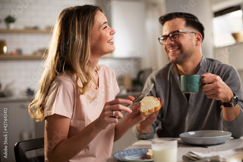 Beautiful woman enjoying in breakfast with boyfriend. Happy young couple drinking coffee and eating sandwich at home.