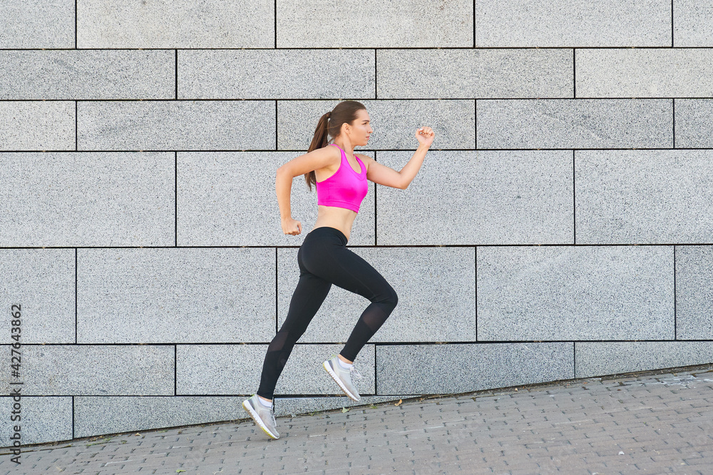 Fototapeta premium Beautiful young woman in sports clothing running while exercising outdoors.
