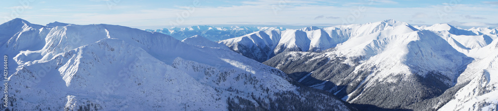 Magnificent panoramic shot of mountain peaks covered in snow during the winter season. A blue sky with few white clouds can be seen in the background. Zakopane - Kasprowy Wierch