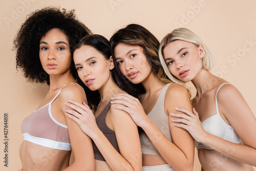 pretty multiethnic women leaning on each other while looking at camera on beige © LIGHTFIELD STUDIOS