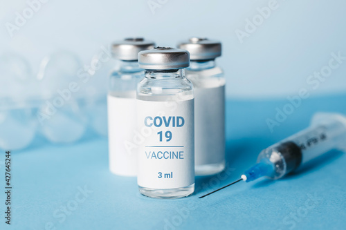 Coronavirus vaccine. Three ampoules with coronavirus vaccine and a syringe on blue background. Covid-19 treatment