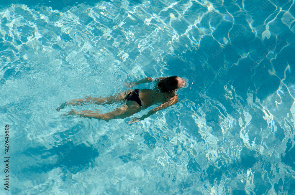 woman in bikini swimming in crystal clear water in a blue colored pool, top view