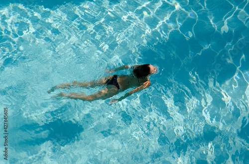 woman in bikini swimming in crystal clear water in a blue colored pool, top view