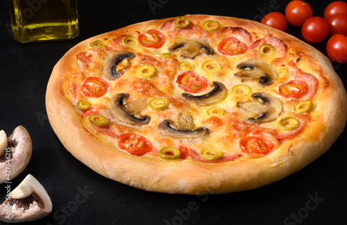 Pizza with tomatoes, mozzarella, salami, mushrooms, oil on black background
