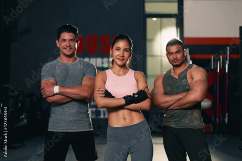 Group of determined multi ethnic people at gym standing strongly with smart pose. Young adult fit Asian woman Asian man and Caucasian man in sportswear at the gym hall.