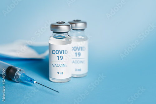 Coronavirus vaccine. Ampoules with coronavirus vaccine and a syringe on blue background. Covid-19 treatment. Copy space