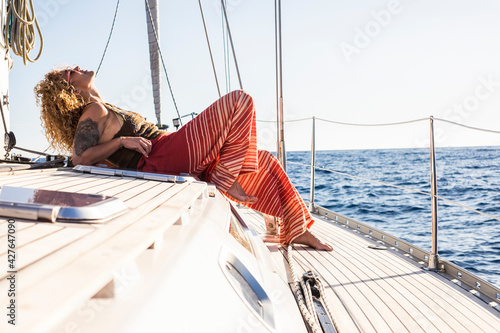 Attractive woman sailing on a yacht on summer day - relax and vacation lifestyle female people laying on the deck of the sailboat enjoying the sun and freedom - blue ocean background photo