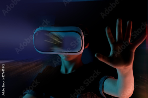 boy, child in dark room with neon lights in modern VR glasses interacting with network while having virtual reality experience, concept study of another world, modern teaching technologies