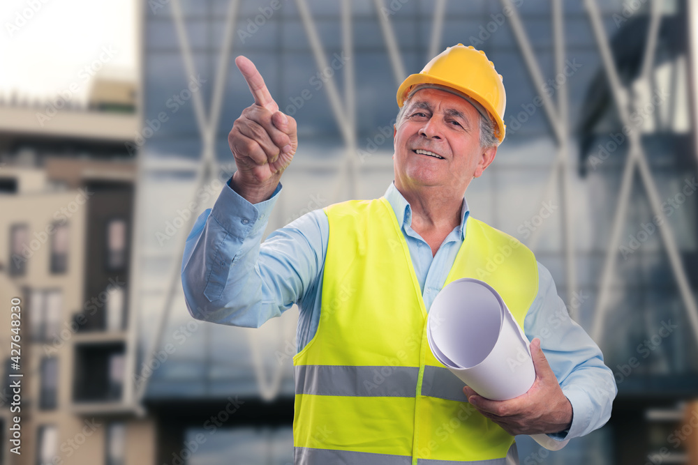 Friendly contractor holding sketches pointing index finger Friendly contractor holding sketches pointing index finger