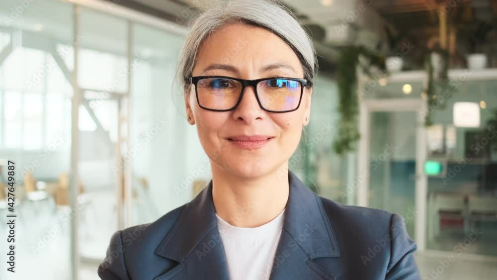 A smiling elder businesswoman is posing to the camera standing in a hall A smiling elder businesswoman is posing to the camera standing in a hall