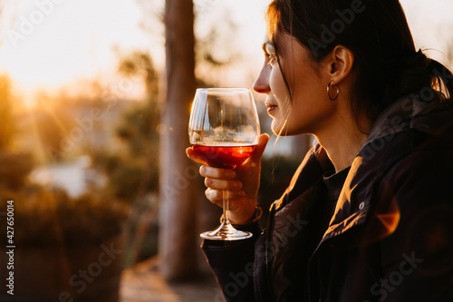 Young woman with a glass of red wine in sunset light at a terrace.