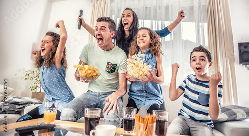 Fotografie Family watching sports match on tv at home, cheering and shouting goal with hand
