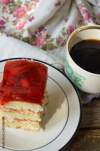 Fototapeta Naklejka Na Ścianę i Meble -  sponge cake with strawberry jelly on top on a plate and a mug of black coffee