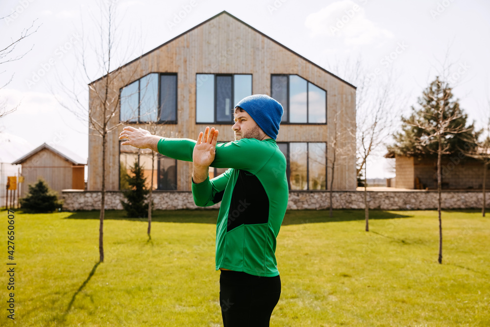Naklejka premium Man working out outdoors in the morning in backyard at home. Man stretching arms.