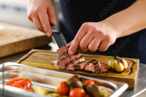 The male chef serves a meat dish and decorates steak. The restaurant's kitchen.