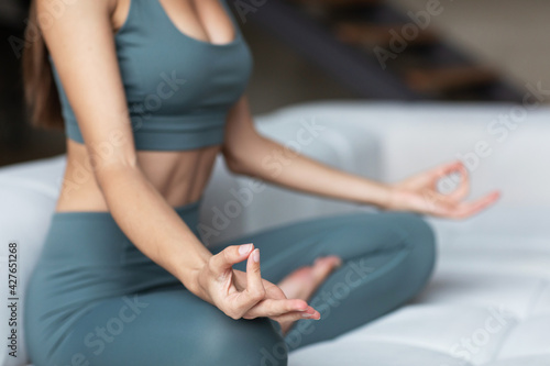 Close-up healthy woman in sportswear meditates in lotus position at home, to be in harmony with body and soul.