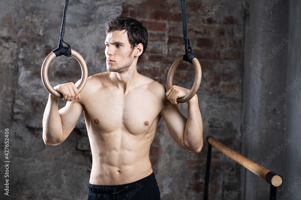 Handsome sporty man in good shape with gymnastic rings