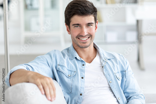 Smiling young man in a denim shirt sitting on the couch living room