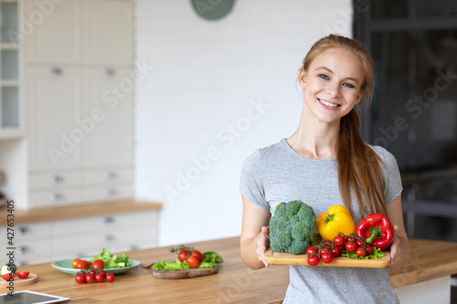 Beautiful healthy woman in the kitchen holds vegetables.