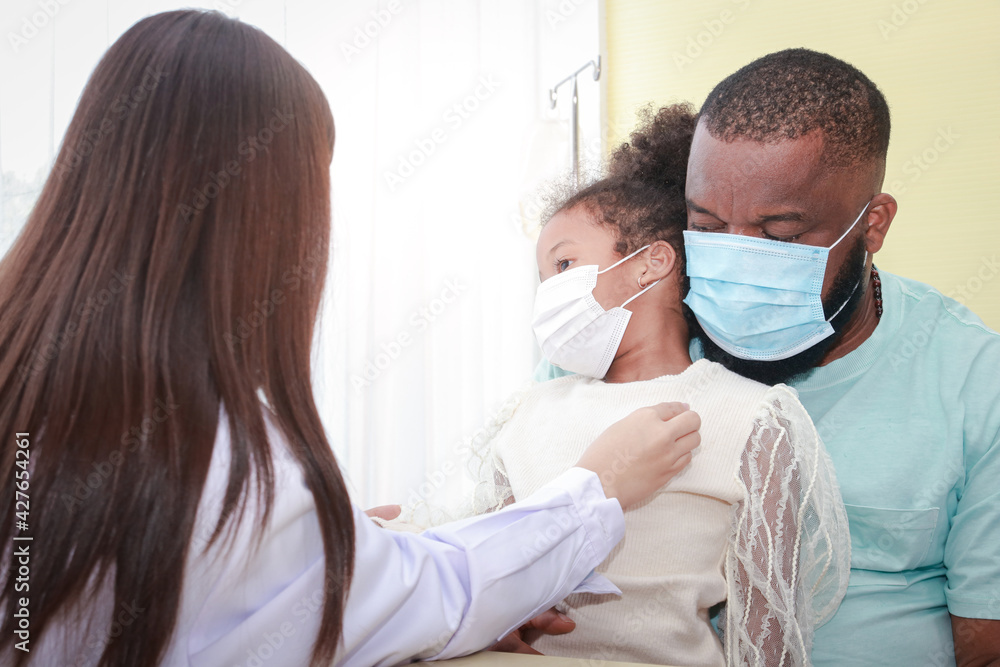 Asian female doctor uses a stethoscope Check the heartbeat of a little African-American girl sitting with her father. Concept of treatment for infectious diseases in children, during Coronavirus Asian female doctor uses a stethoscope Check the heartbeat of a little African-American girl sitting with her father. Concept of treatment for infectious diseases in children, during Coronavirus