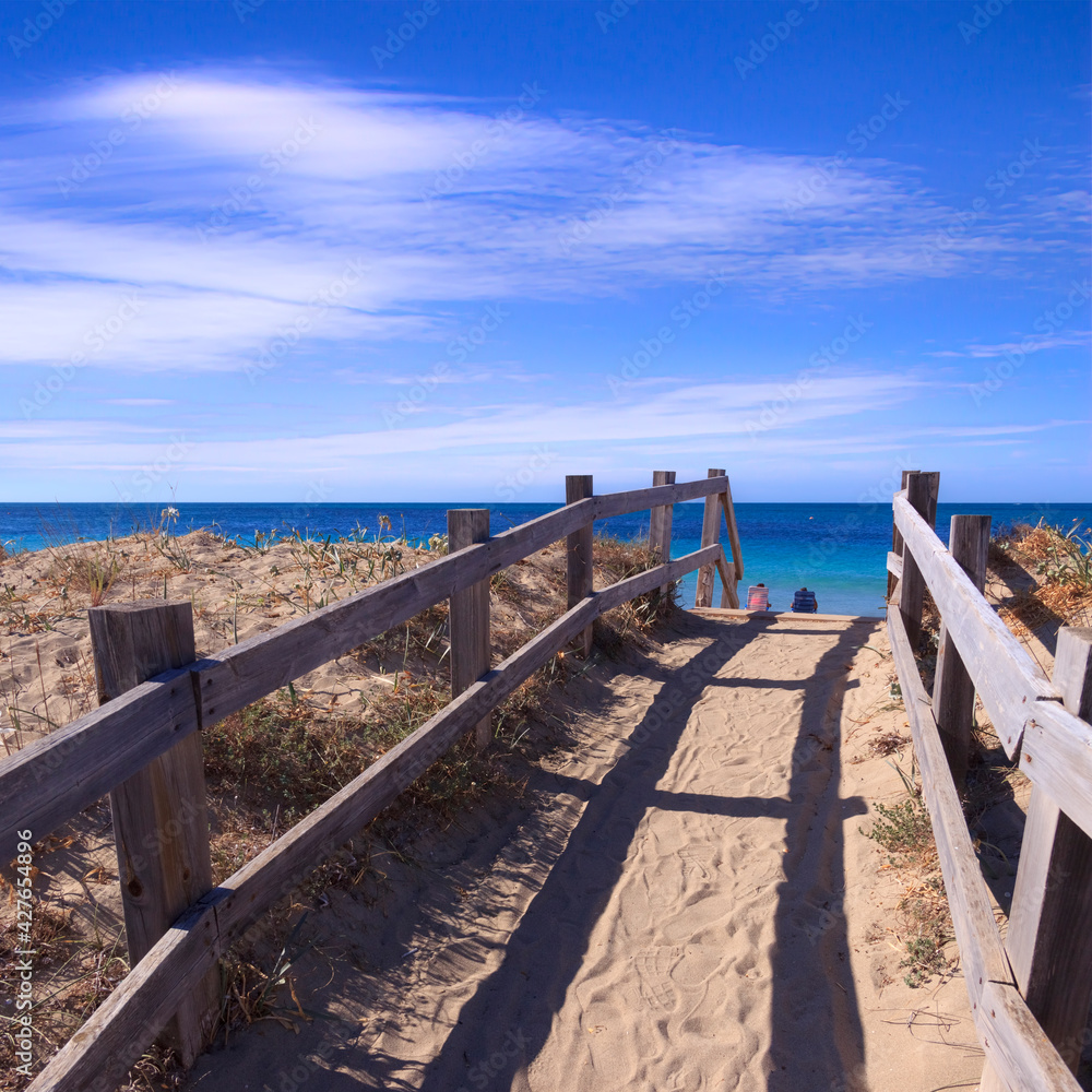 Boardwalk on the beach: fence between sea dunes in Salento, Apulia (Italy). Tourists sitting on deck chairs.