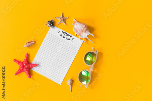 Beach accessories with summer to do list notebook, sunglasses, sea shell and stars on yellow background. Travel planning concept. Flat lay, copy space