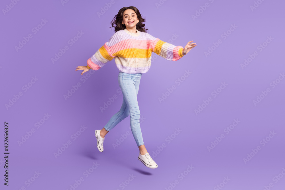 Full size photo of young happy excited girl go walk in air wear knitted sweater and pants isolated on purple color background Full size photo of young happy excited girl go walk in air wear knitted sweater and pants isolated on purple color background