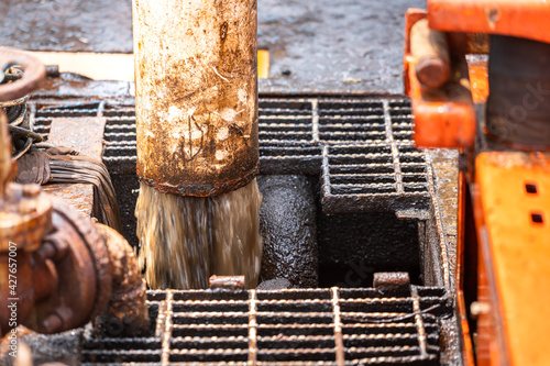 Chemical and oil contaminated water is draining out from piping to the treatment process. Close-up and selective focus at piping part. Industrial equipment and processing concept photo.