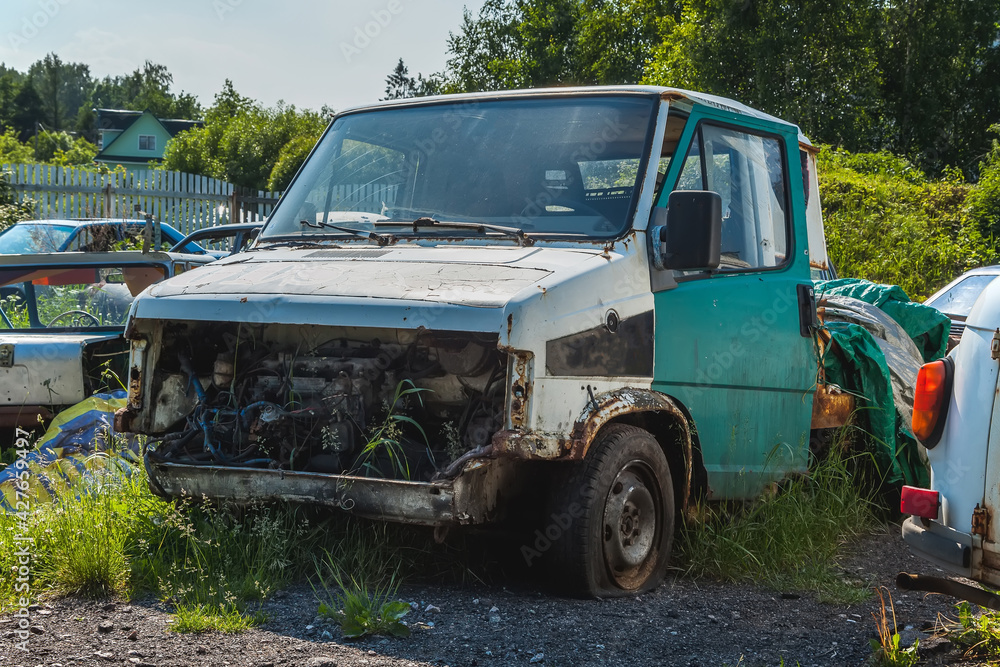 A rusty broken-down car with flat tires stands in the trash. Dump of various cars outside the city. Disassembly of vehicles for spare parts. Cemetery of cars.