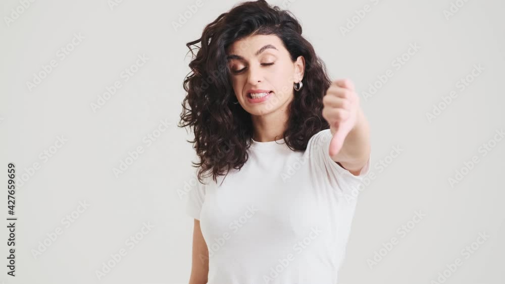 The upset woman showing thumb-down to the camera while standing in the studio The upset woman showing thumb-down to the camera while standing in the studio