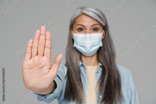 Mature white-haired woman in face mask showing stop gesture