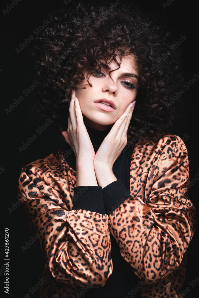 Fashionable portrait of a white Caucasian girl with African curls. Girl in a leopard-print jacket on a black background. Fashionable portrait of a white Caucasian girl with African curls. Girl in a leopard-print jacket on a black background.