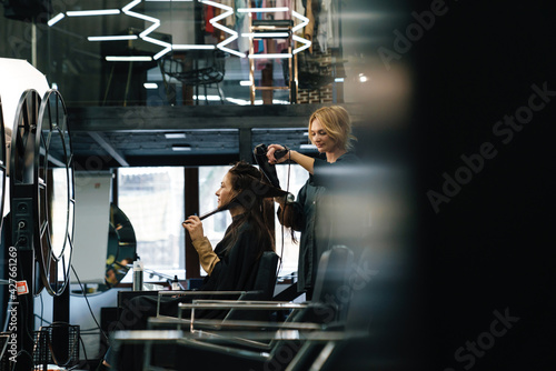 Young blonde woman doing hairstyle for her client in beauty salon
