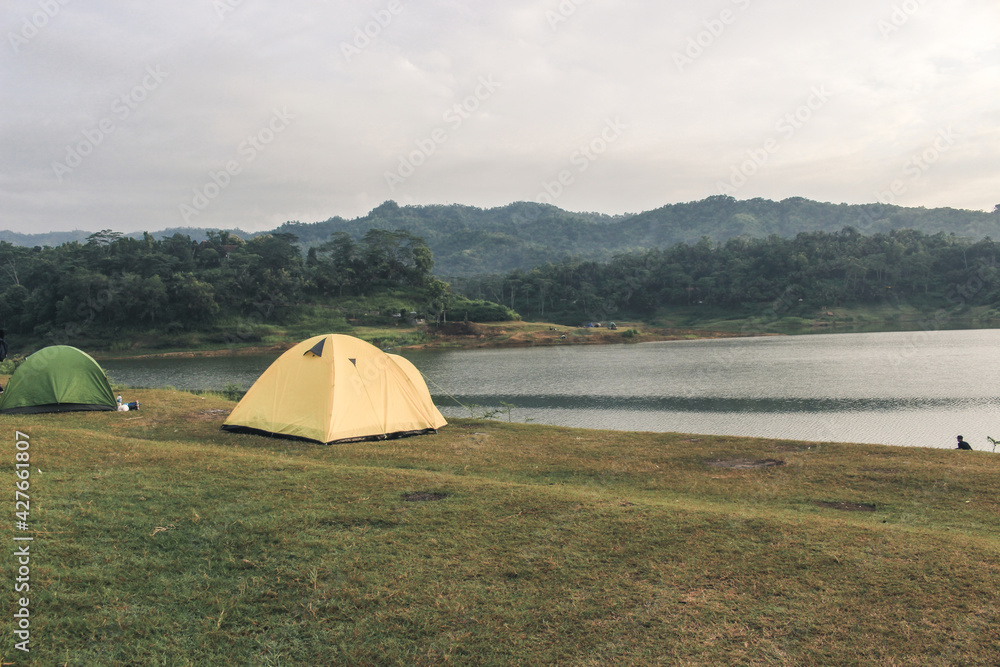 The yellow tent stands in the grasslands overlooking the lake