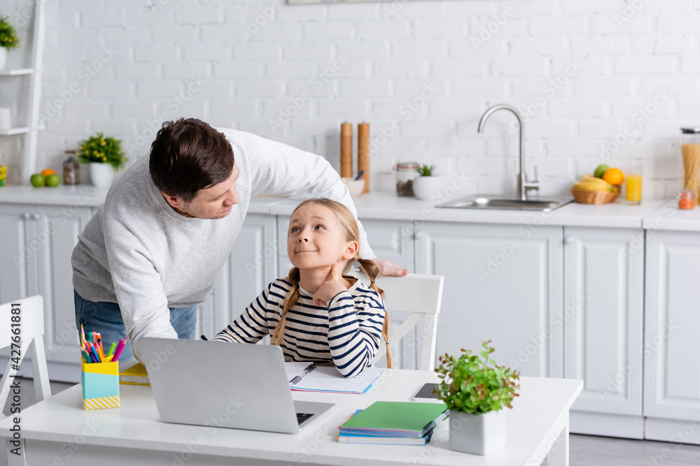 father and daughter looking at each other during online lesson in kitchen father and daughter looking at each other during online lesson in kitchen