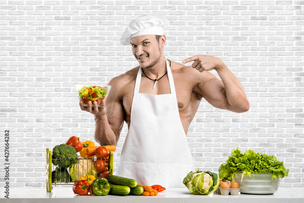 Man bodybuilder in white toque blanche and cook protective apron Man bodybuilder in white toque blanche and cook protective apron